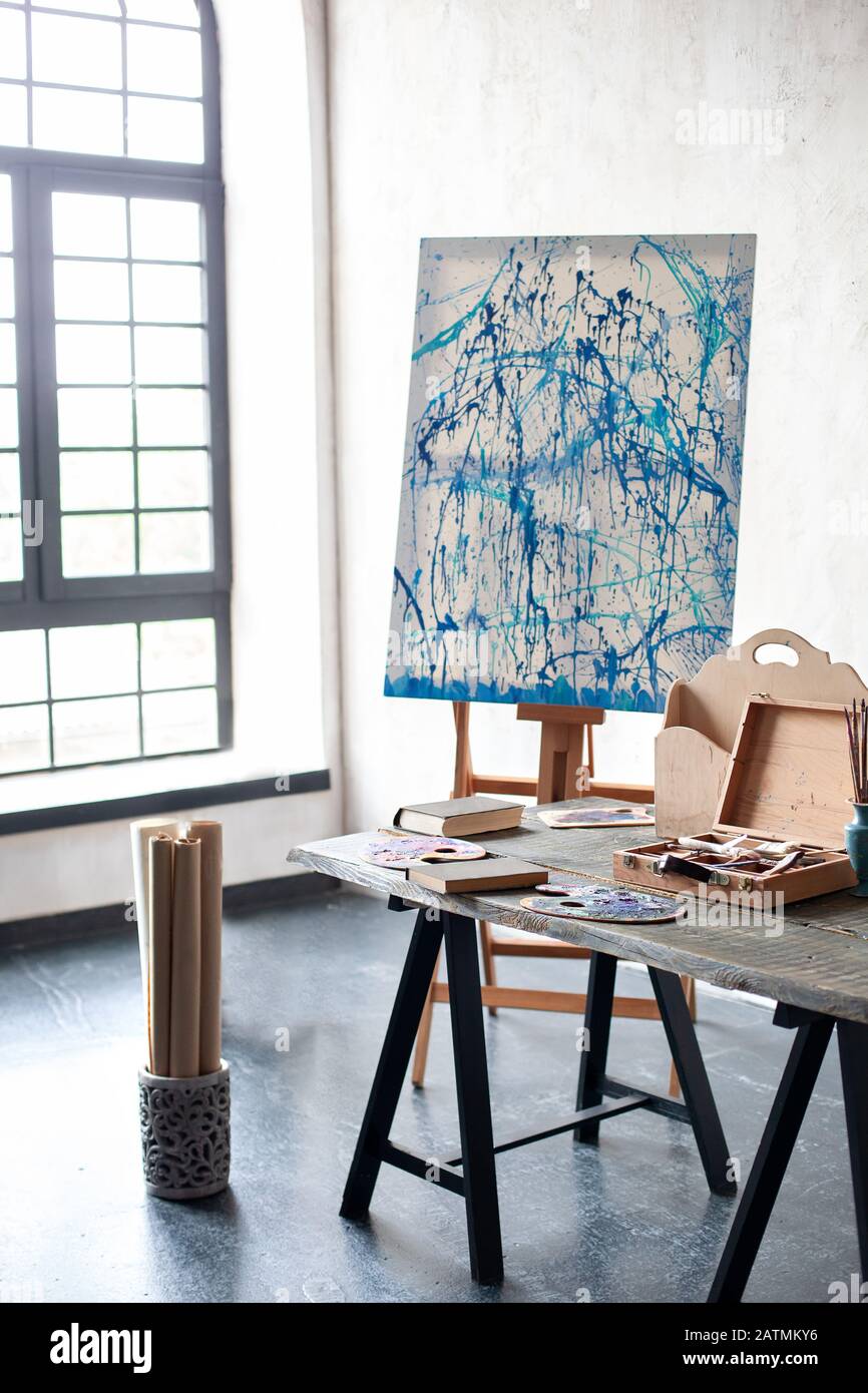 Easel, canvas, brushes, pencils, paints with albums on the table. The