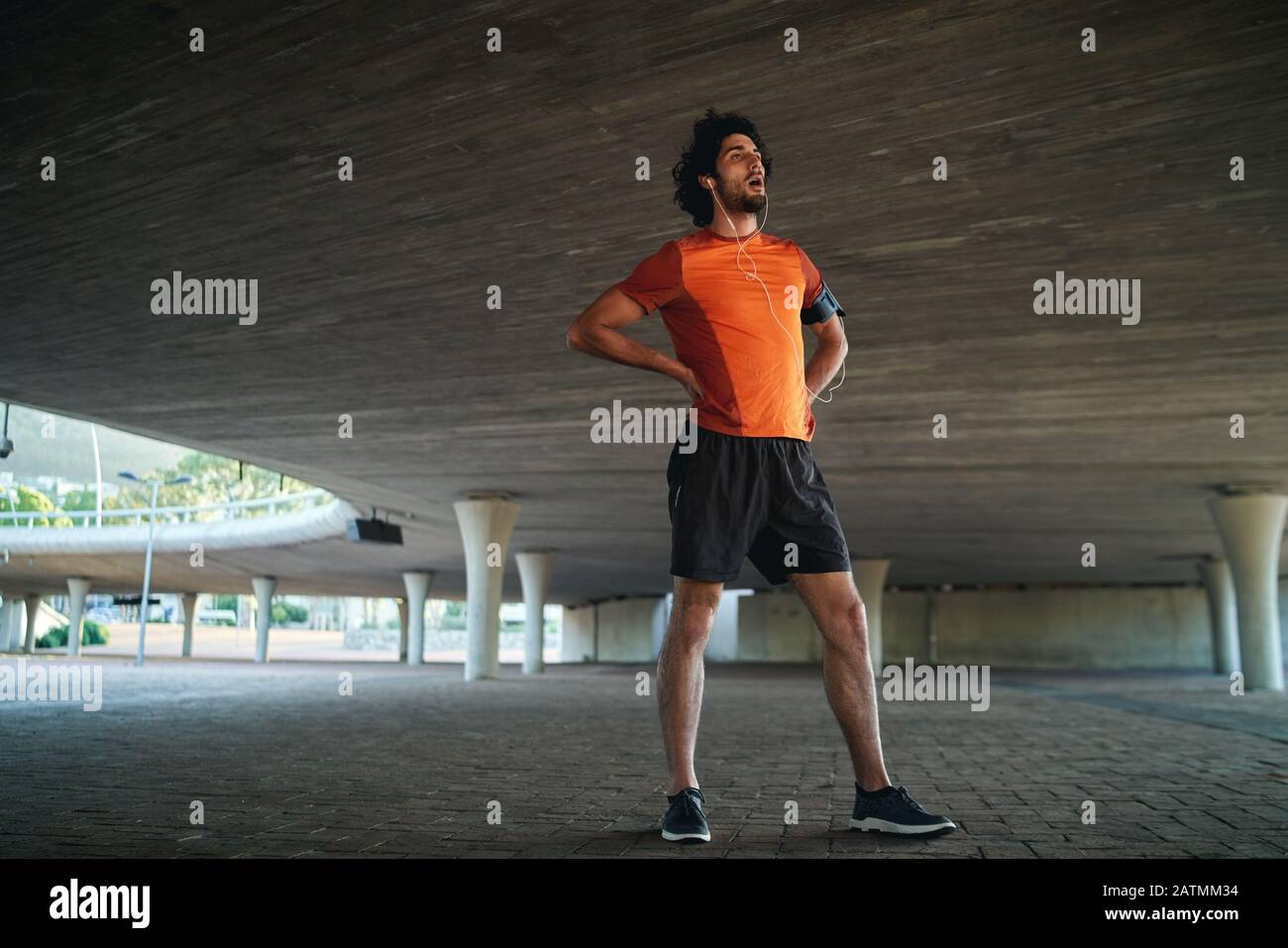 Young caucasian male fitness man resting after work out with his hands on hip standing under the bridge - fit male taking a breather Stock Photo