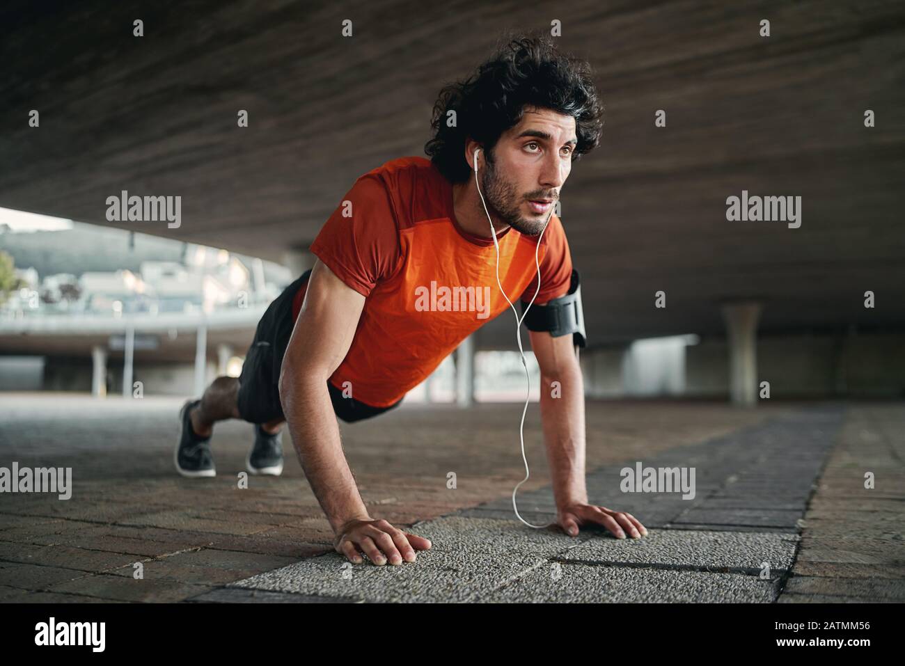 Attractive fit man listening to music in earphone doing push-ups exercises during workout outdoors - man showing perseverance and determination Stock Photo