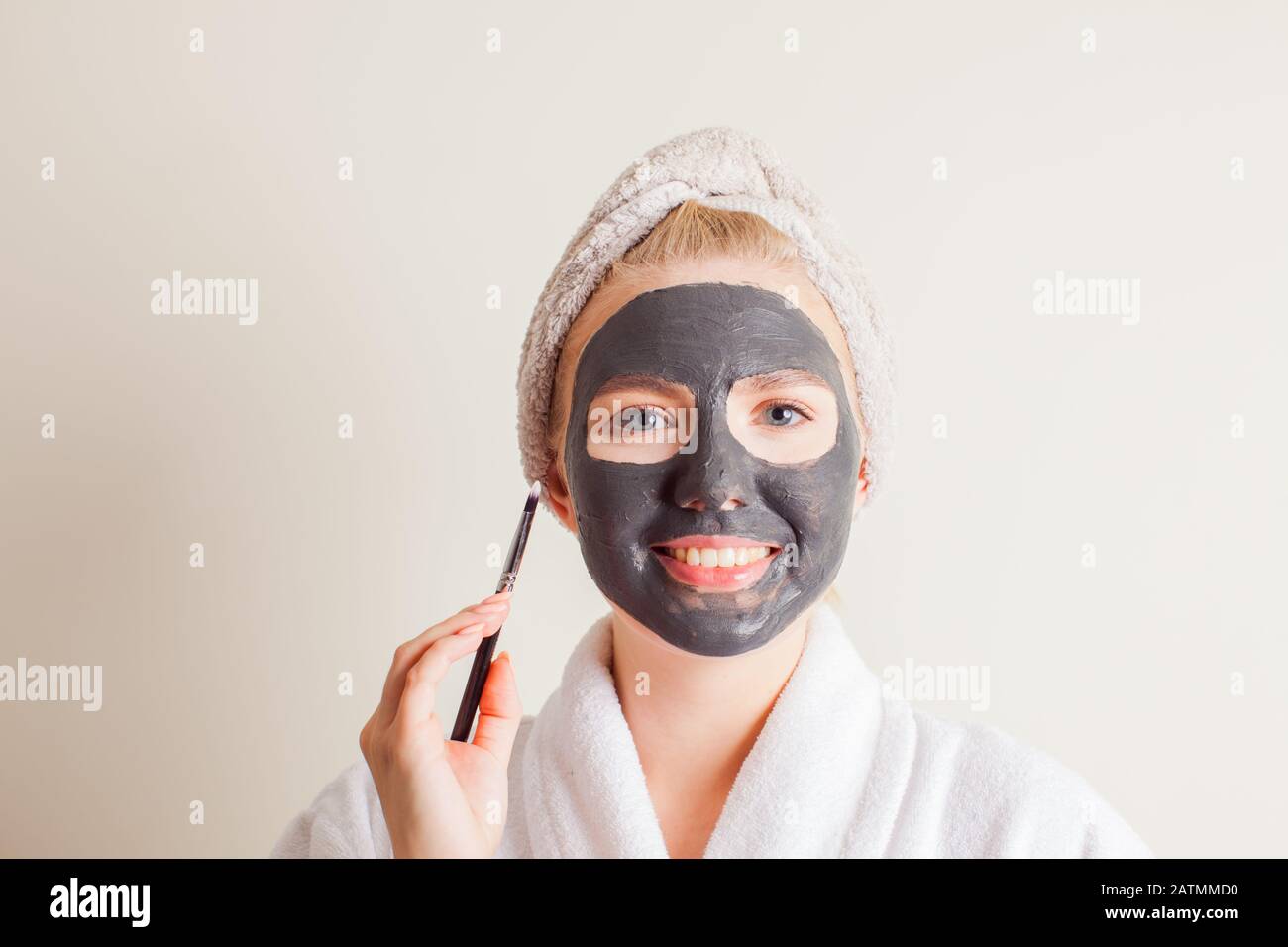 Smiling woman applying black charcoal mask on face Stock Photo