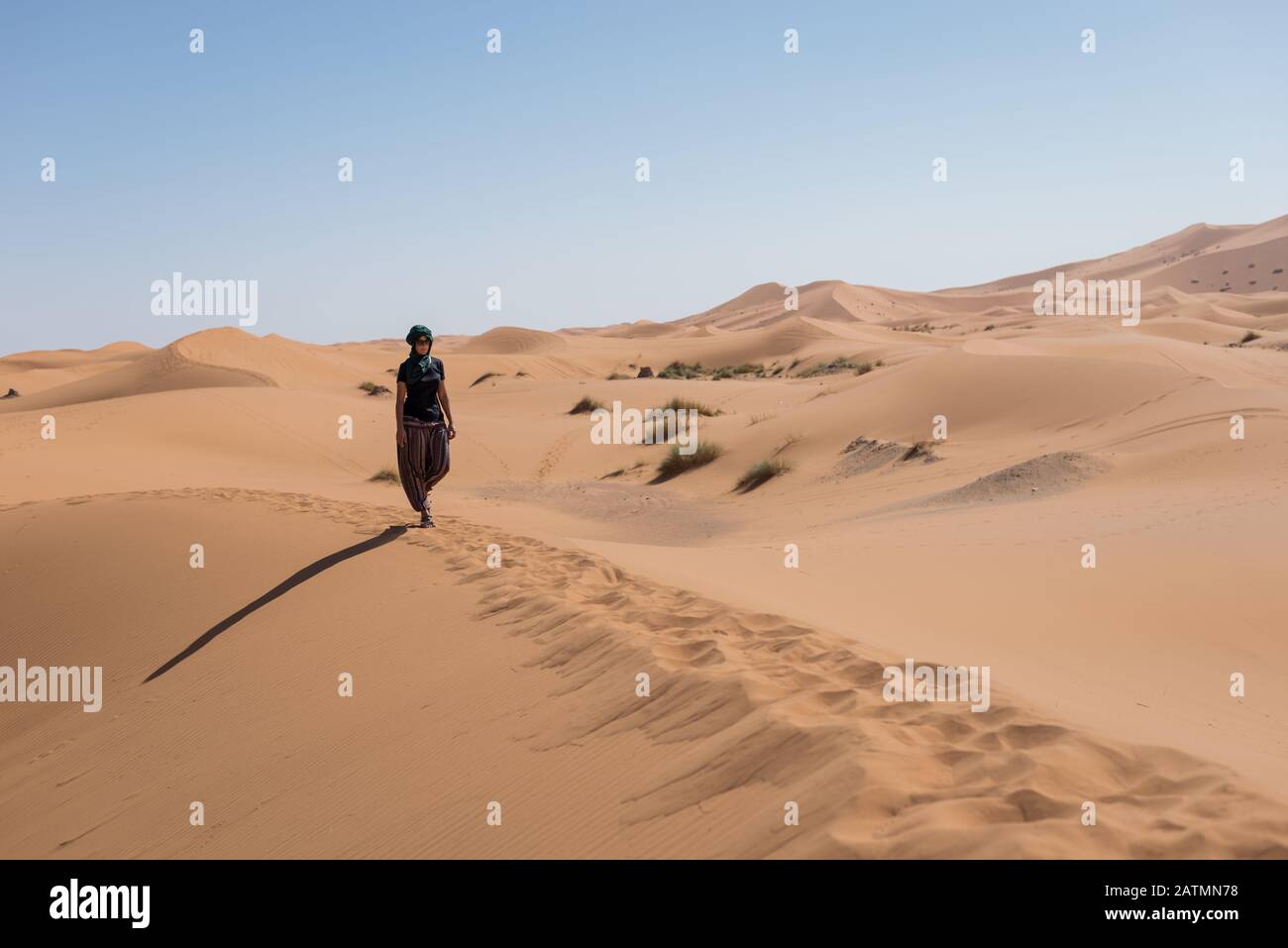 Woman walking in the dunes in the Moroccan Sahara desert. Stock Photo