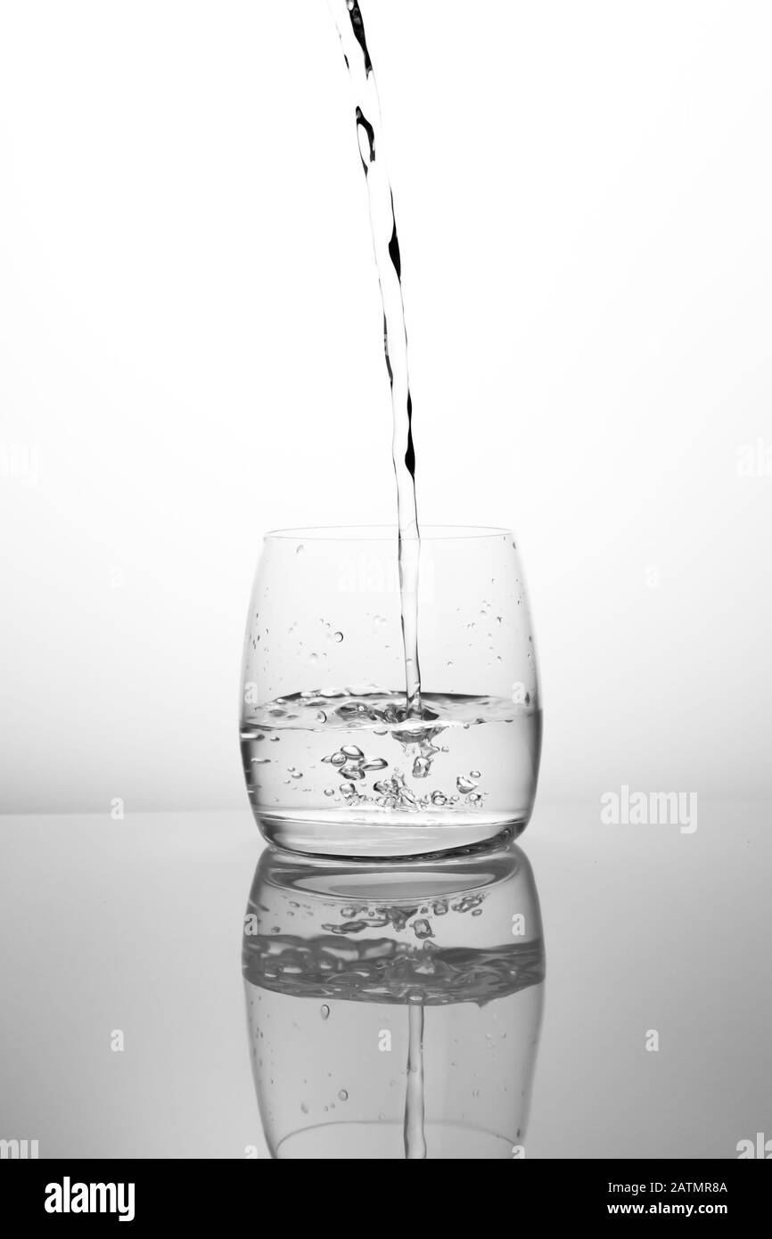 A stream of clean drinking water flows into a transparent glass. Black and white glass with water and natural air bubbles. A bubbling stream of spring Stock Photo