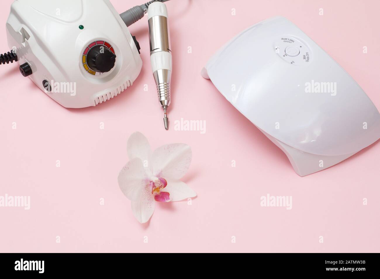 Milling cutter, led UV lamp and orchid flower on a pink background. A set of cosmetic tools for professional hardware manicure. Top view Stock Photo