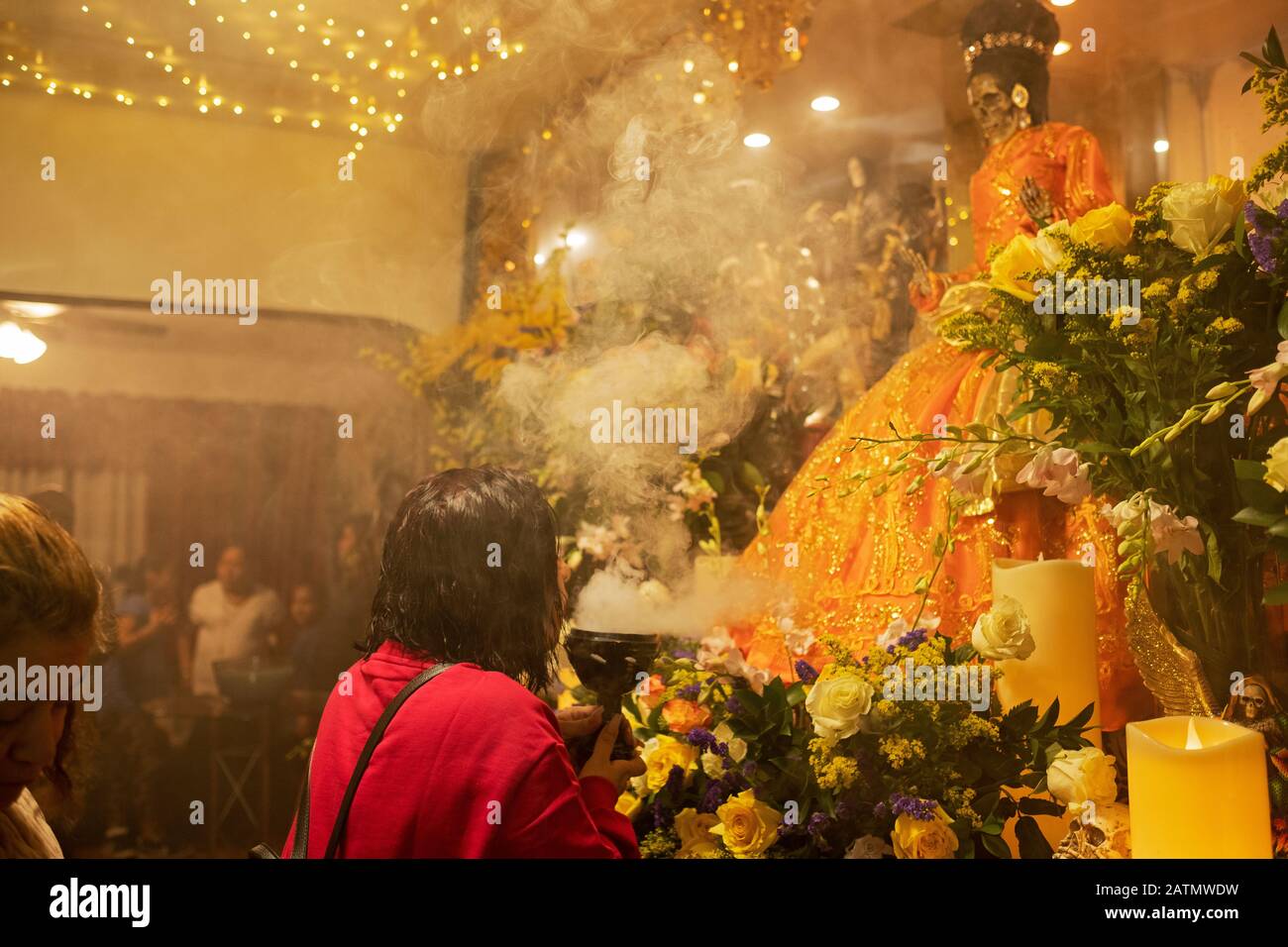A Mexican American worshipper blows smoke at a statue of Santa Muerte in a home temple in Queens, New York City. Stock Photo
