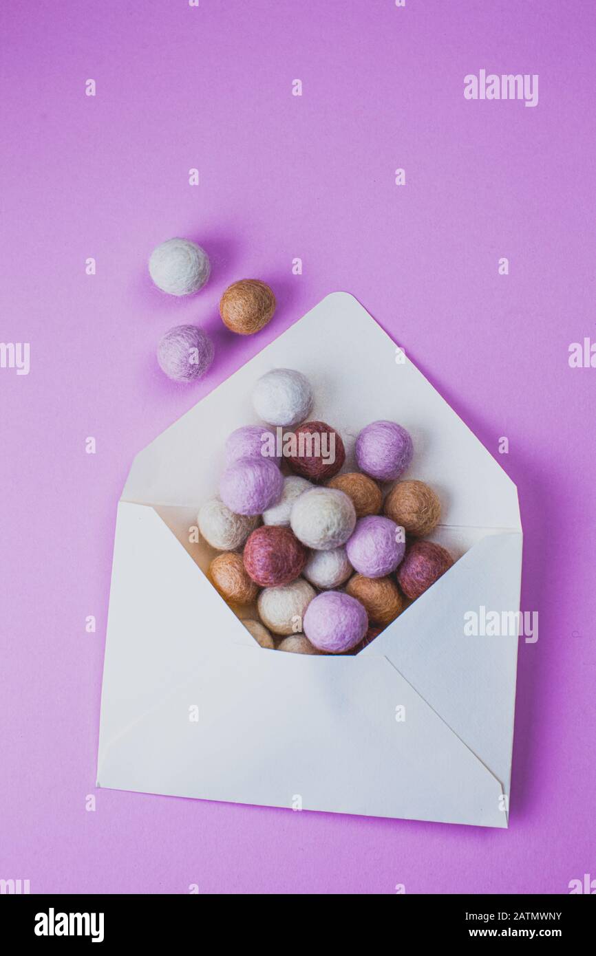 Opened envelope with colorful felt balls on purple background. Minimal style. Stock Photo