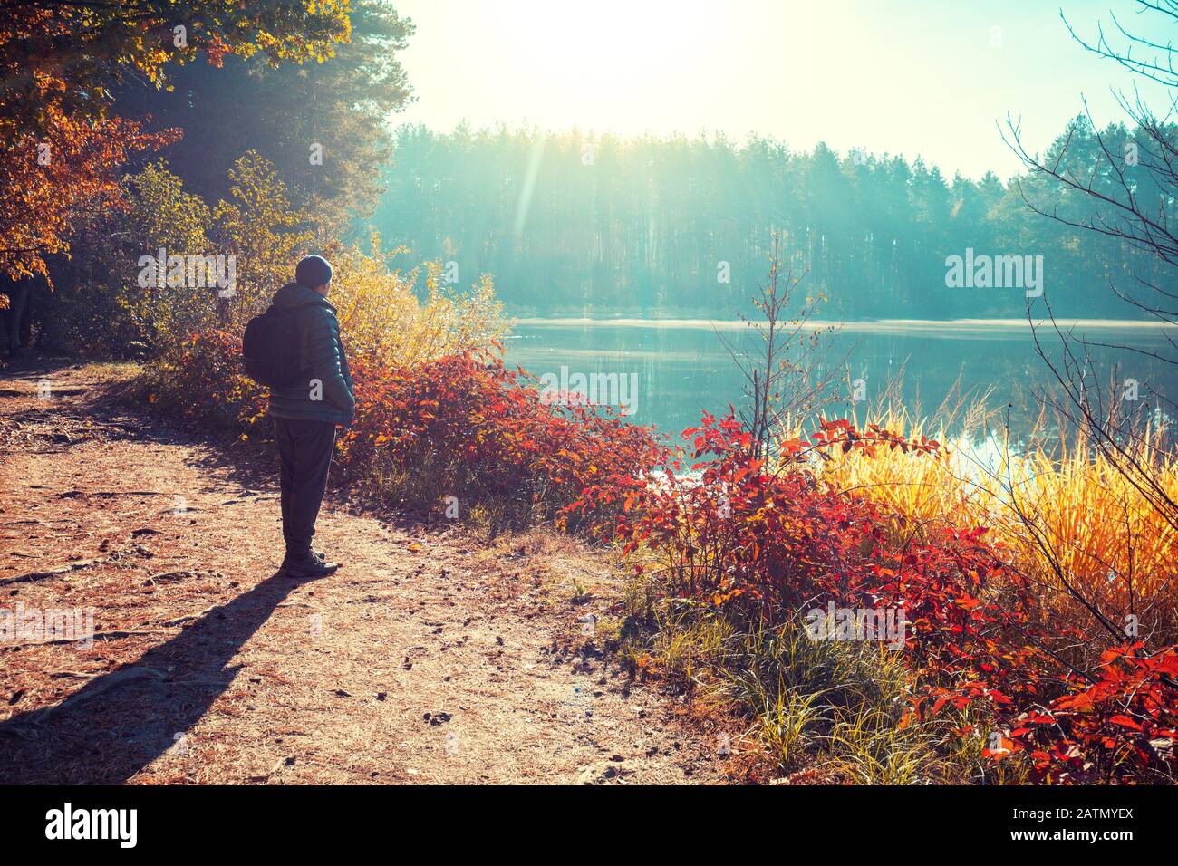 Man tourist stands on a picturesque lakeshore in the autumn morning and looking at the sunrise Stock Photo