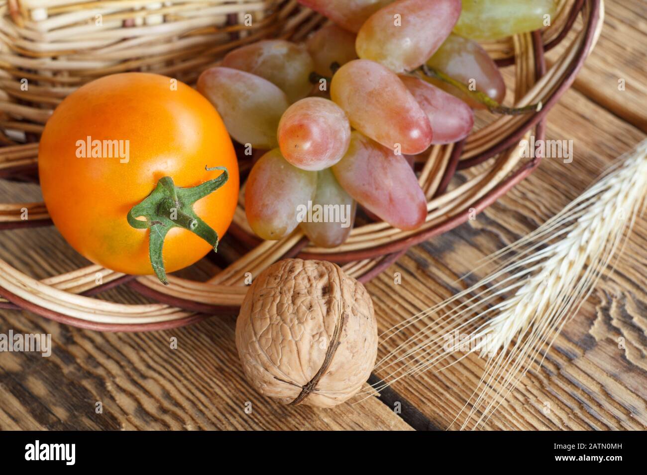 Close-up walnut, tomato, grape and wicker basket on old wooden boards. Shallow depth of field. Top view. Stock Photo
