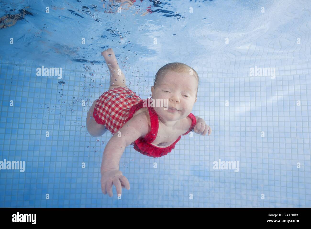 Newborn girl in a red swimsuit learns to dive in a swimming pool Stock Photo