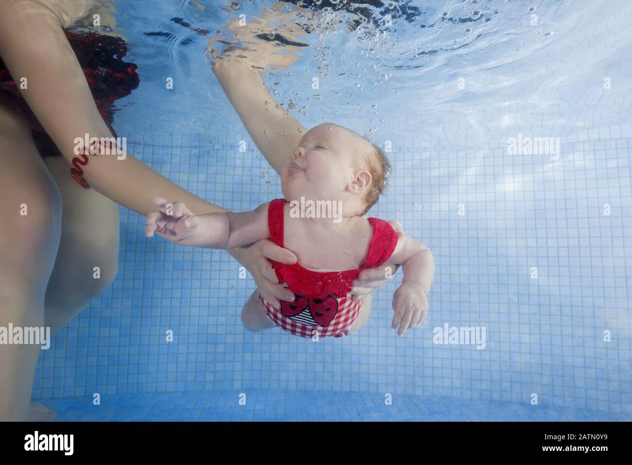 Newborn girl in a red swimsuit learns to dive in a swimming pool