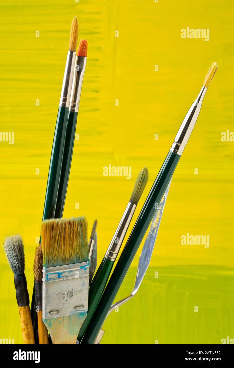 Artistic art supply utensils with paintbrushes on yellow canvas background with selective focus Stock Photo