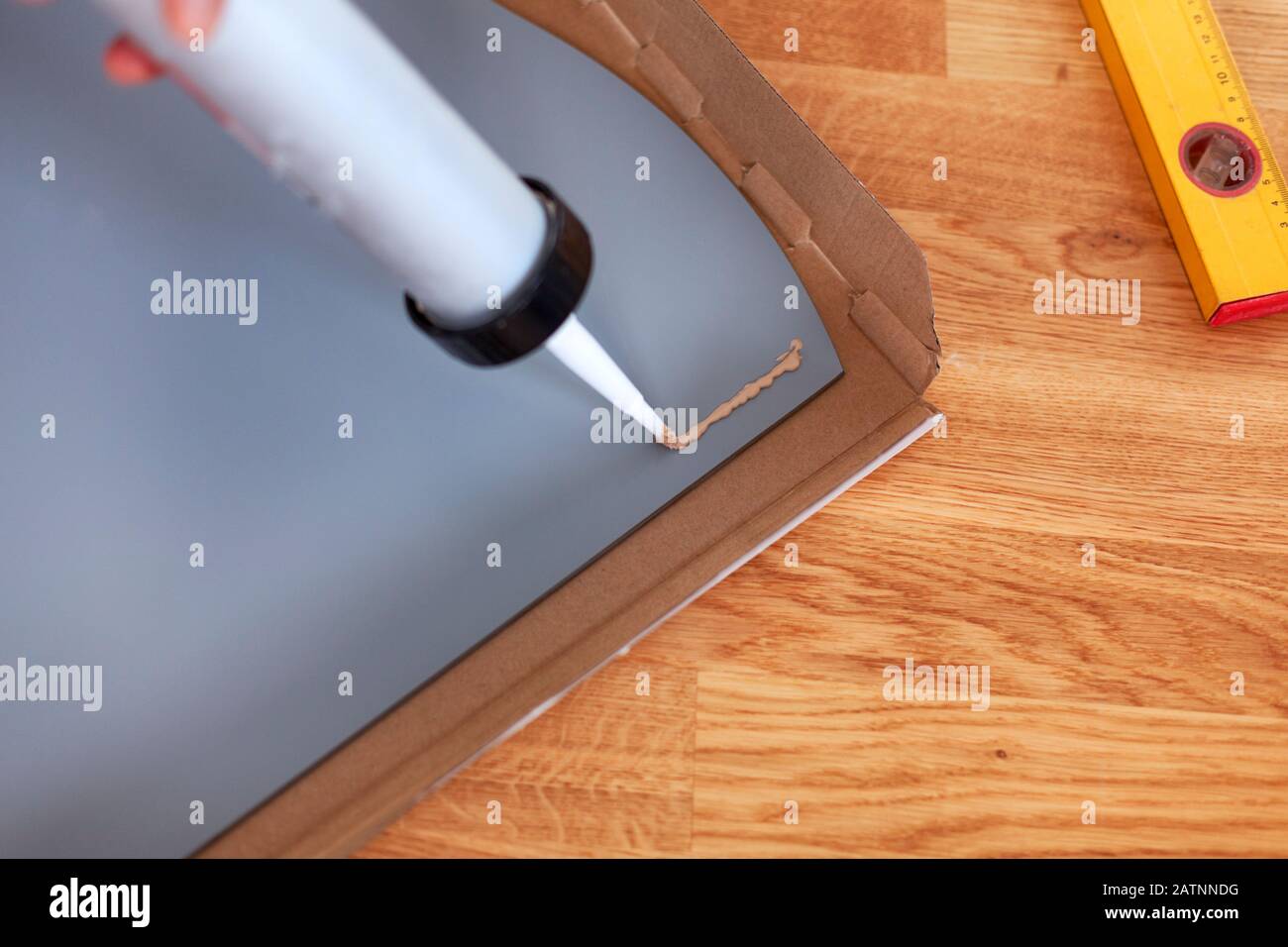 Liquid nails being applied to back of mirror using glue gun on parquet floor. Closeup Stock