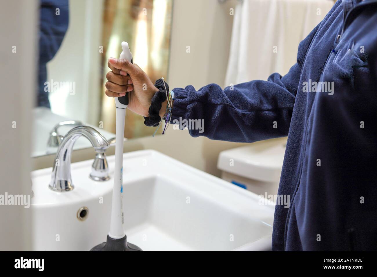 African-American woman using a plunger to fix the bathroom sink Stock Photo  - Alamy