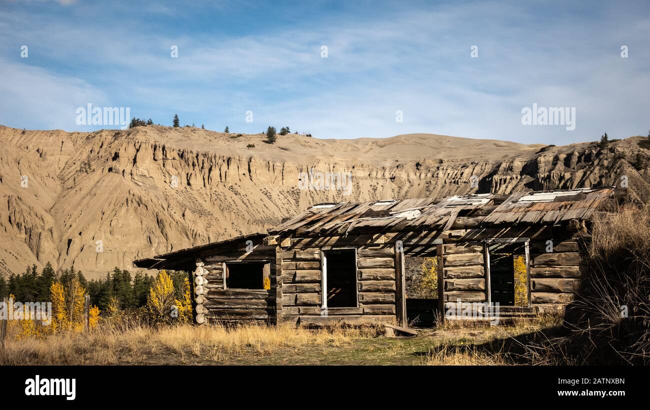 A relict of the first pioneers: The old, rustic building of the Potwell farm in front of the iconic hoodoos and sand dune at Farwell Canyon, BC. Stock Photo