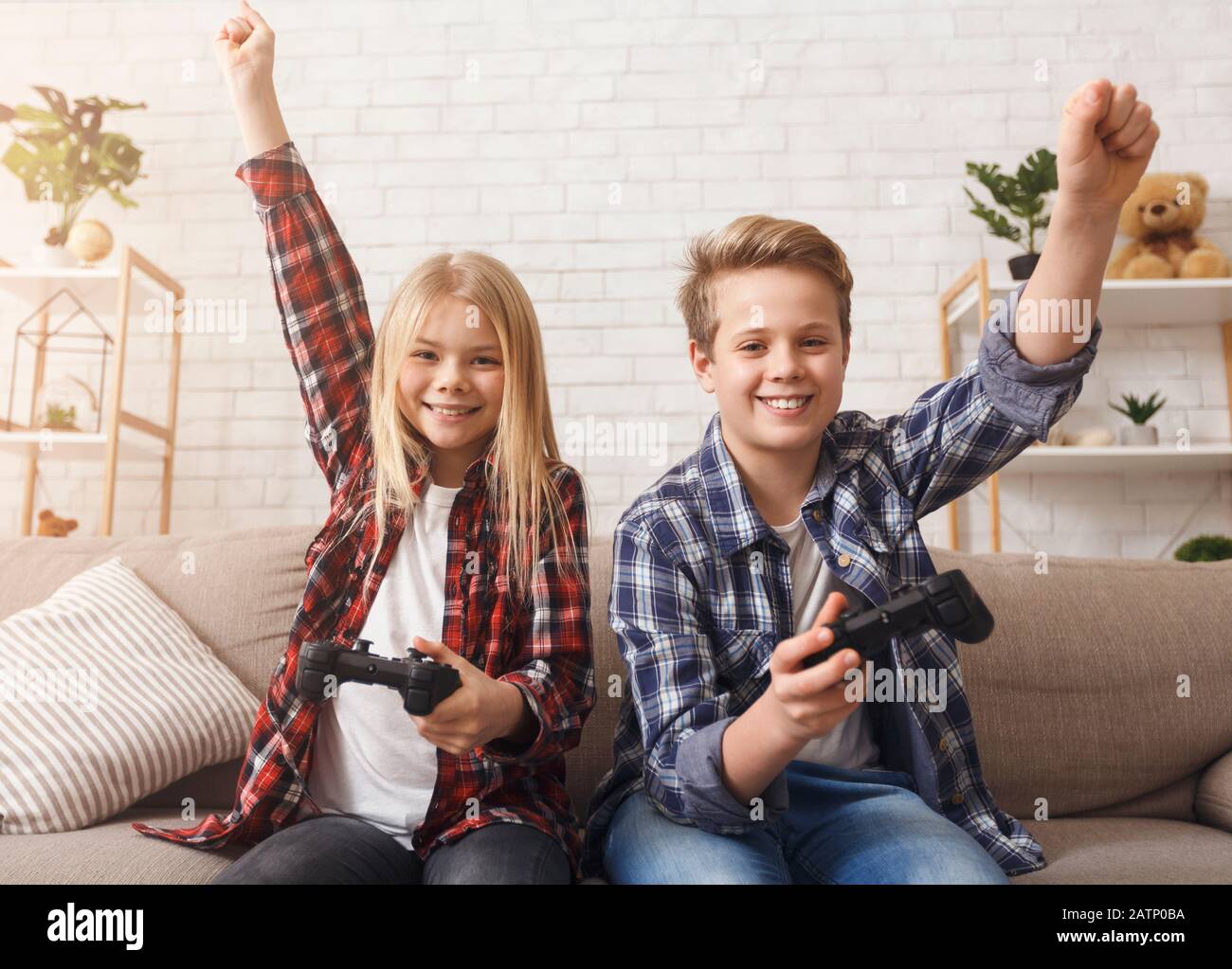 Children Playing Video Game Together Celebrating Victory Sitting On Sofa Stock Photo