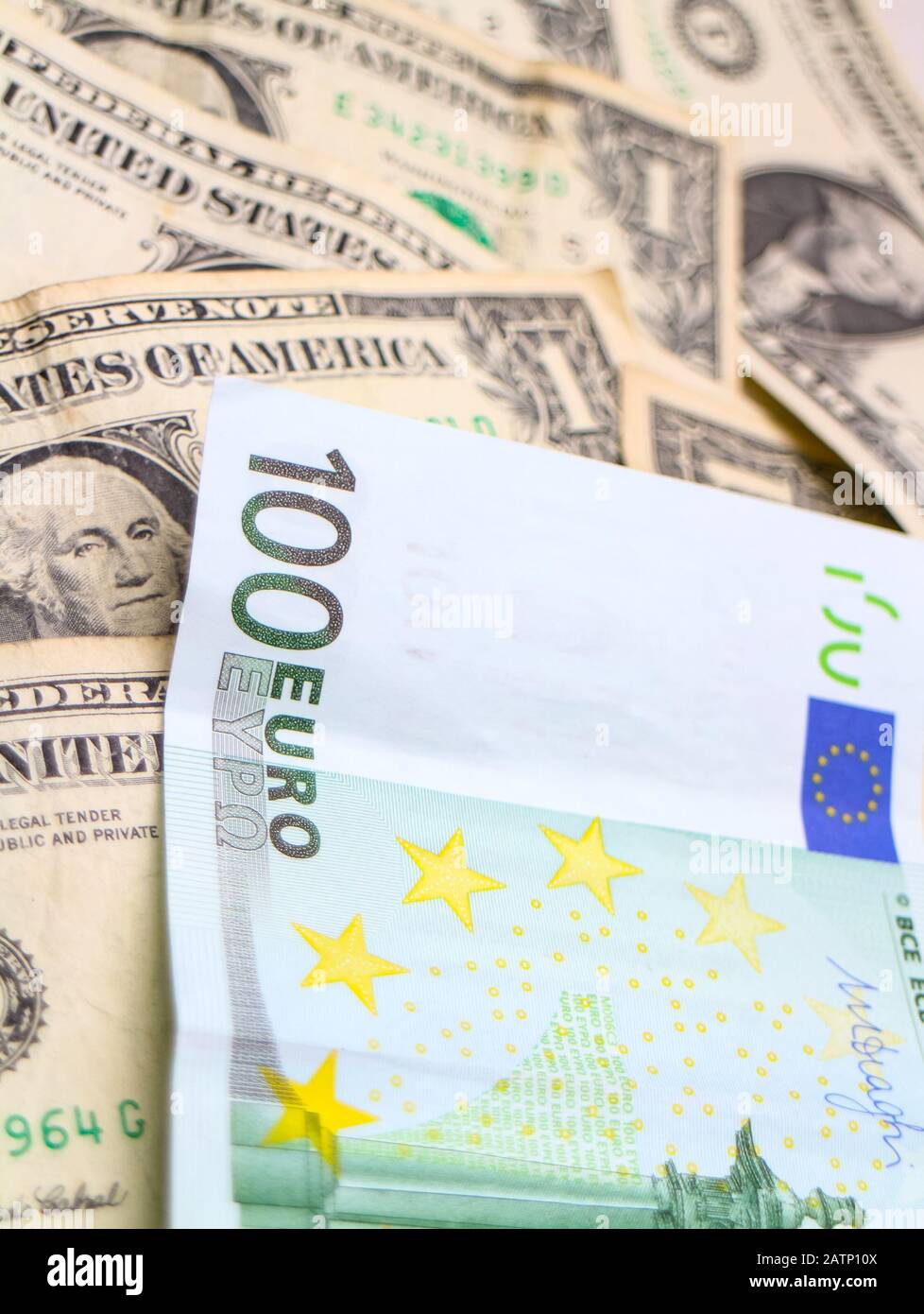 A 100 Euro banknote arranged over a pile of US Dollar banknotes. Stock Photo