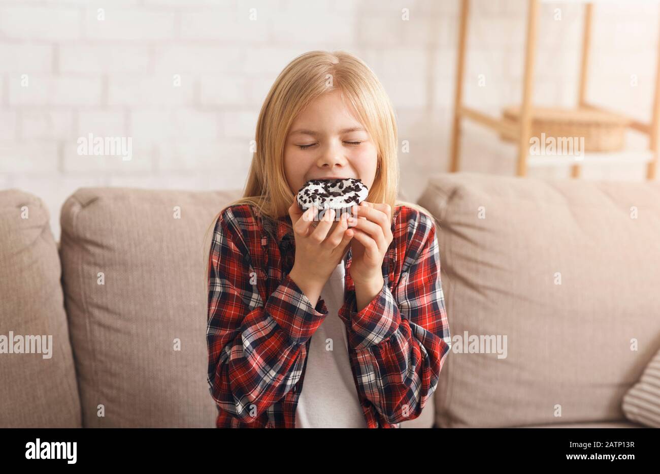 Little Girl Eating Unhealthy Dougnut Dessert Sitting On Couch Indoor Stock Photo