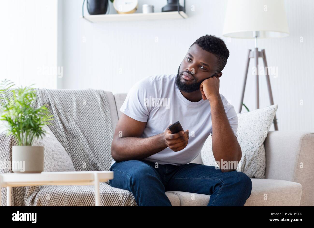 Bored african guy sitting at home, switching tv for film Stock Photo