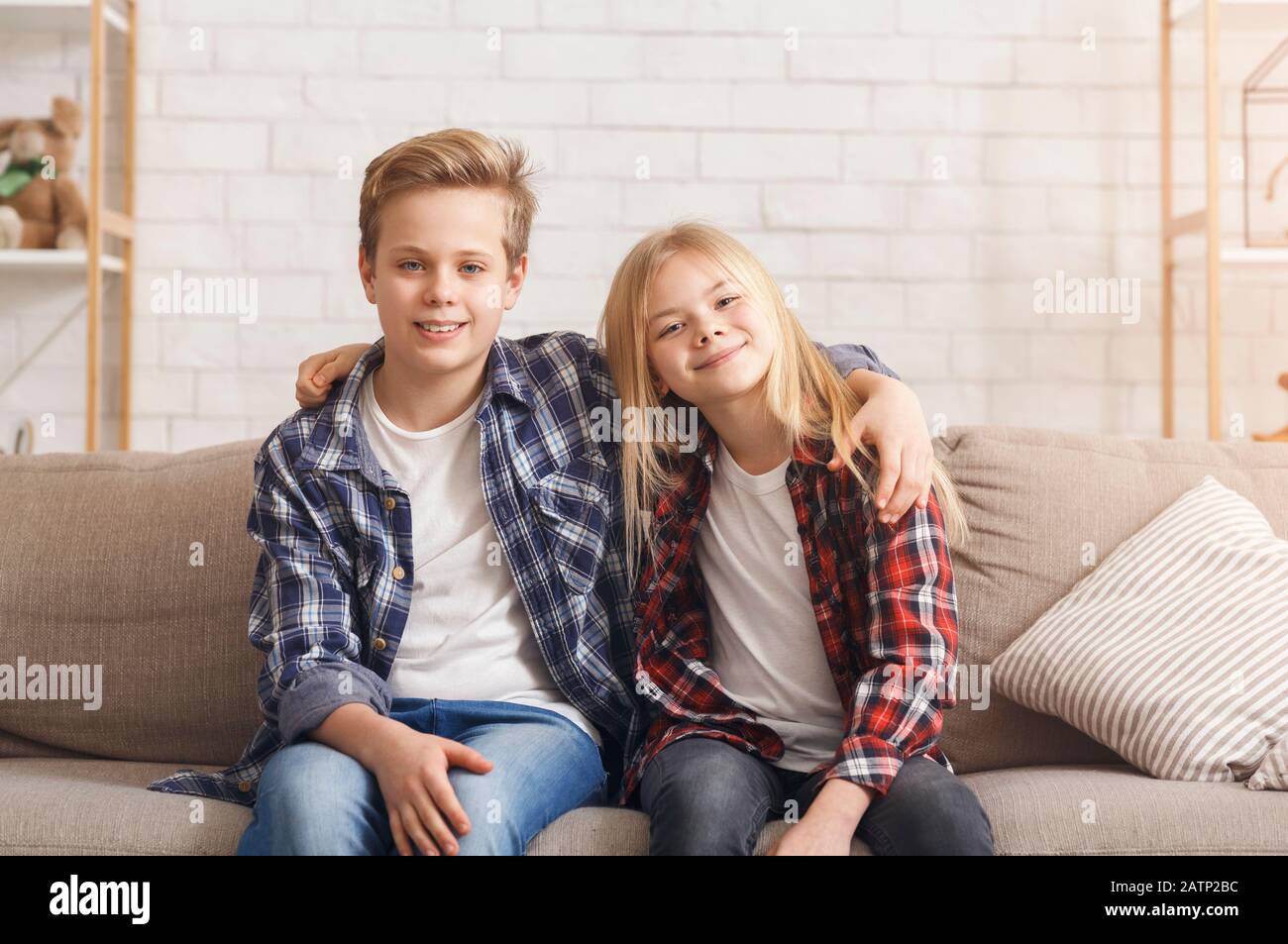 Brother And Sister Embracing Smiling Sitting On Couch At Home Stock Photo