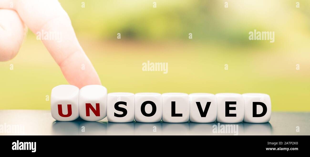 Hand turns dice and changes the word 'unsolved' to 'solved'. Stock Photo