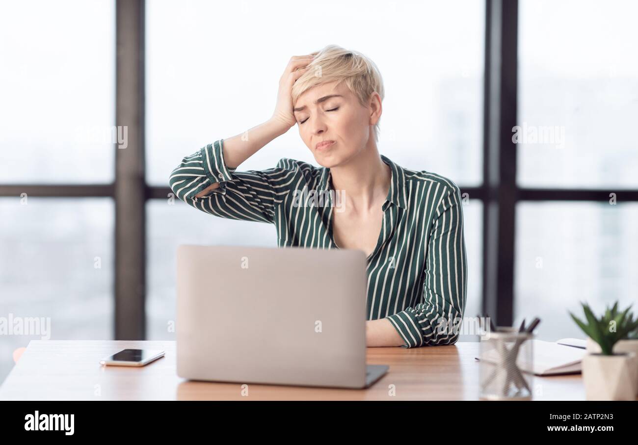 Lady Touching Head Suffering From Pain Sitting In Modern Office Stock Photo
