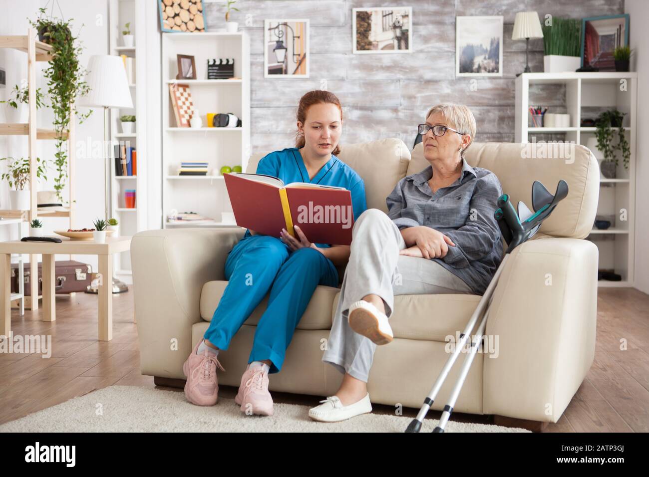 Female care giver reading a story from a book to a senior woman in nursing home. Stock Photo