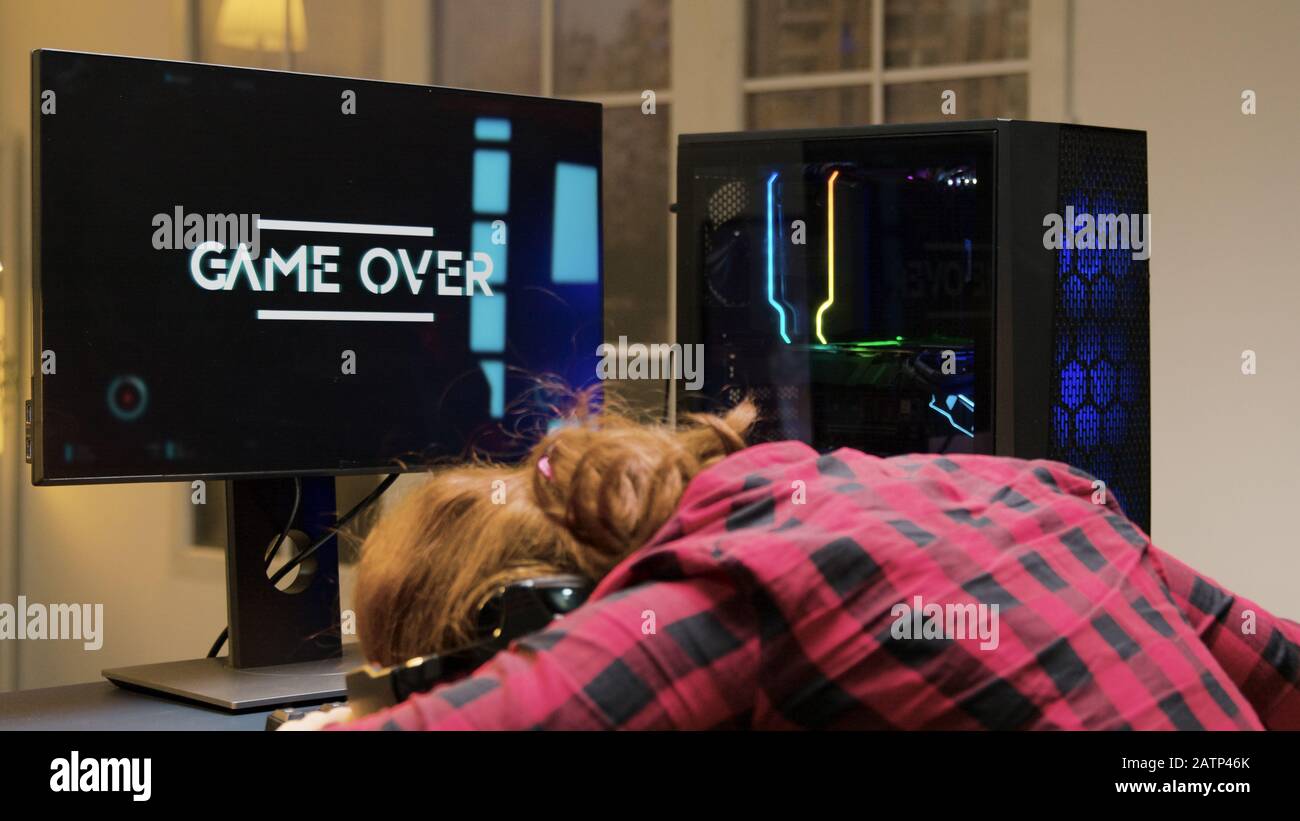 Woman with head on desk after losing a gaming competition. Game over for female gamer. Stock Photo