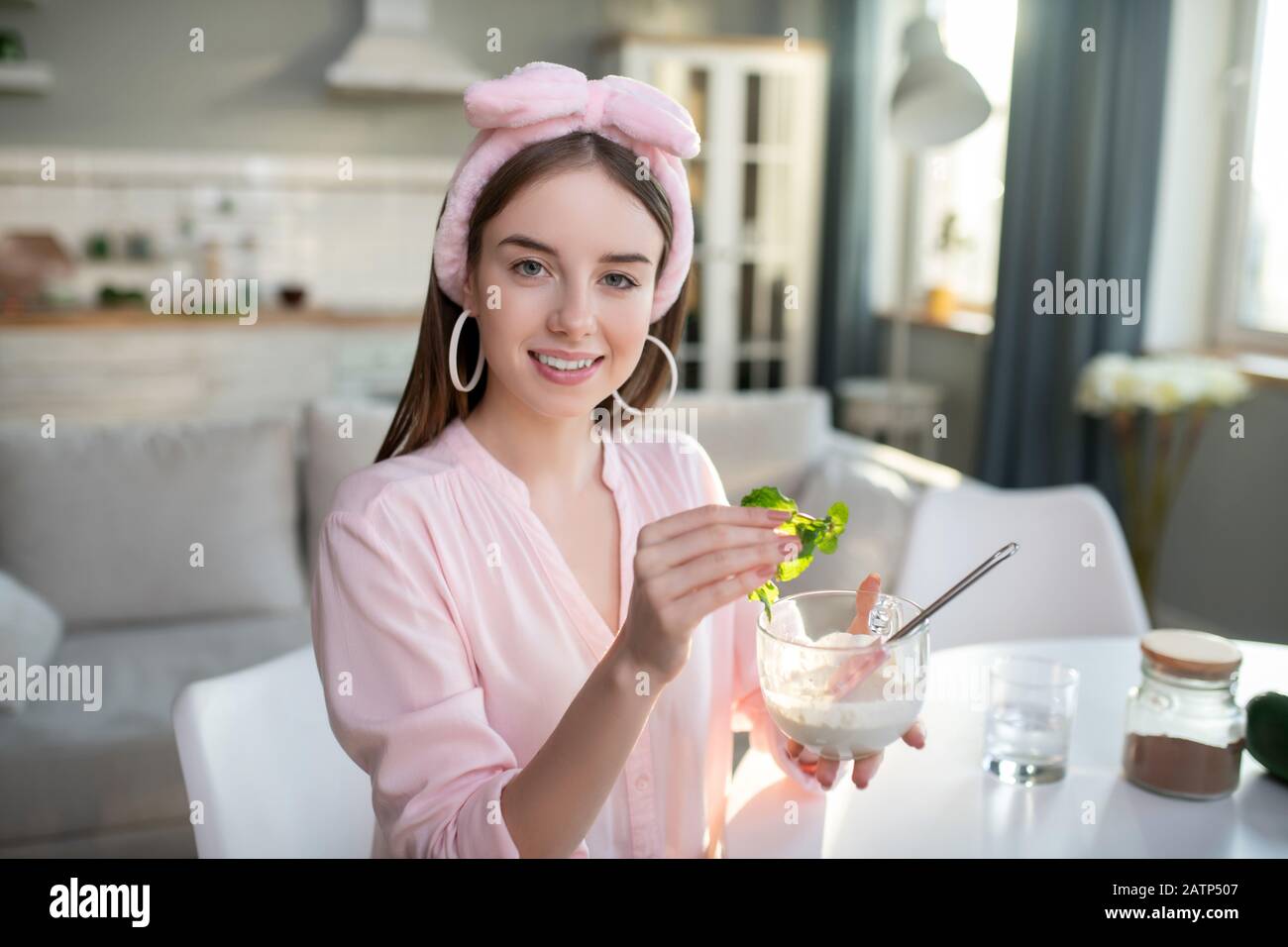 Young pretty girl in a pink headband making a home-made facial mask Stock Photo