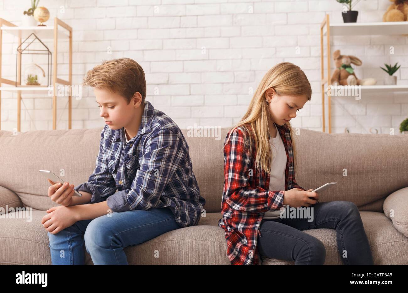 Brother And Sister Using Phones Sitting On Couch At Home Stock Photo