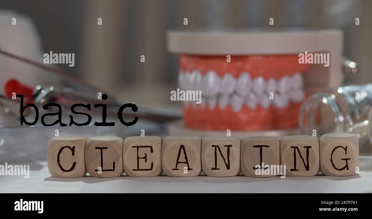 Word BASIC CLEANING composed of wooden dices. Pills, documents, pen, human jaw model in the background. Closeup Stock Photo