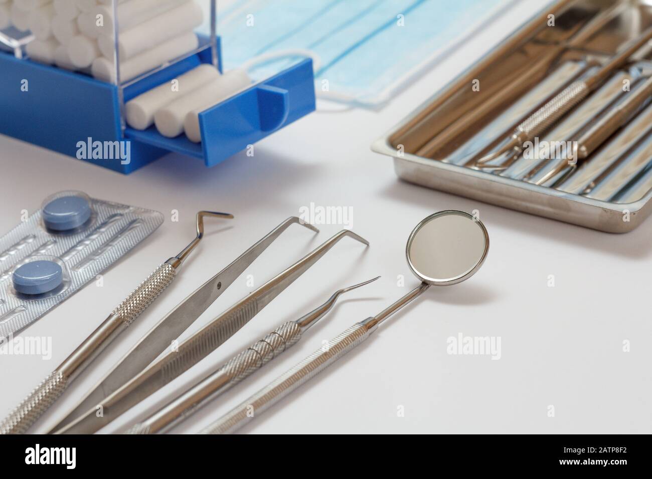 Set of metal dental instruments for dental treatment on white background. Medical tools in stainless steel tray with cotton tampons holder and pills. Stock Photo