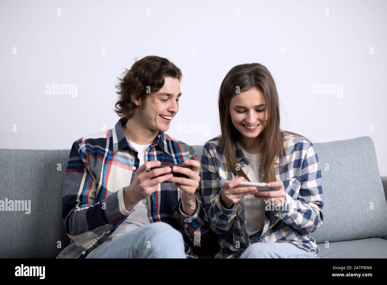Cheerful couple laughing while using smartphones on sofa. Stock Photo