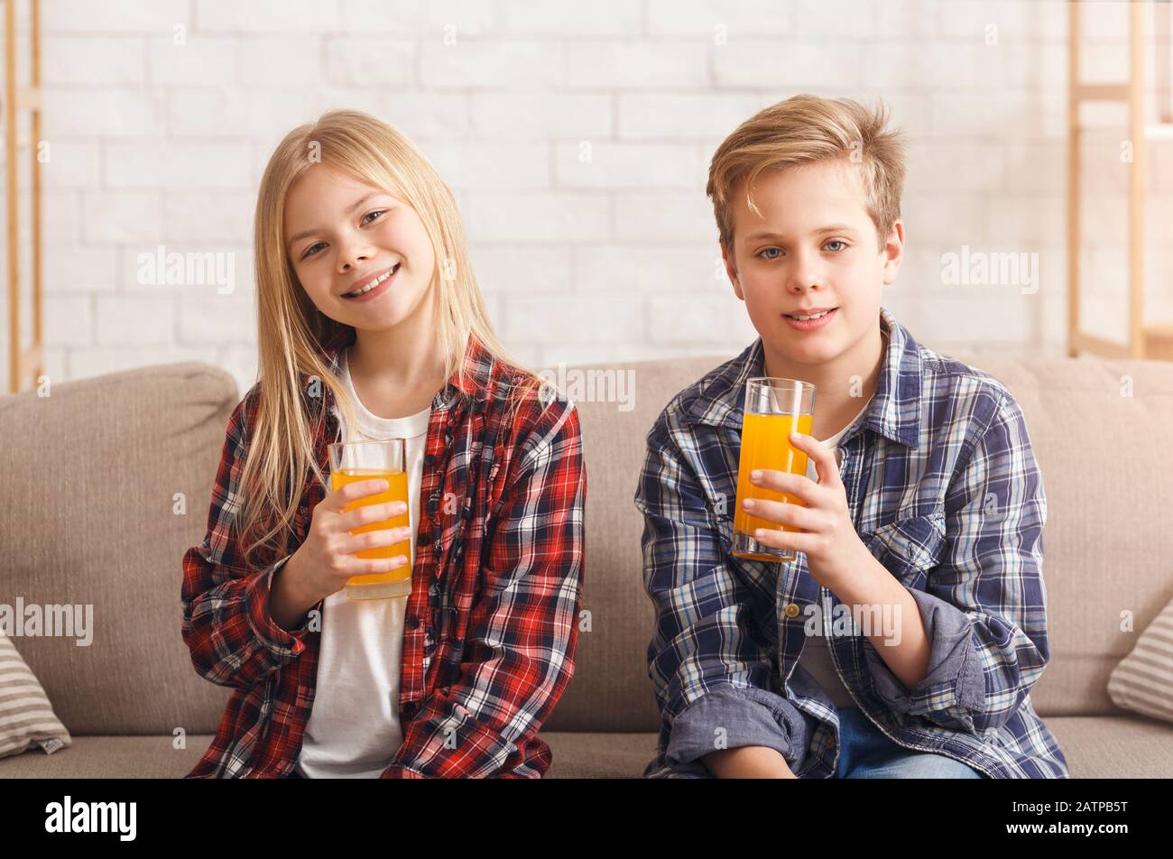 Brother And Sister Drinking Orange Juice Sitting On Sofa Indoor Stock Photo