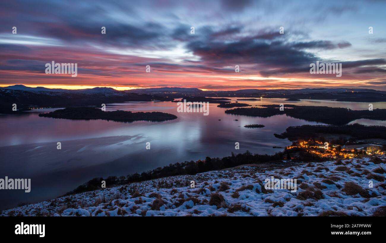 Sunrise on a cloudy, winter morning over the village of Luss and Loch Lomond as seen from the slopes of Beinn Dubh, Scotland. Stock Photo