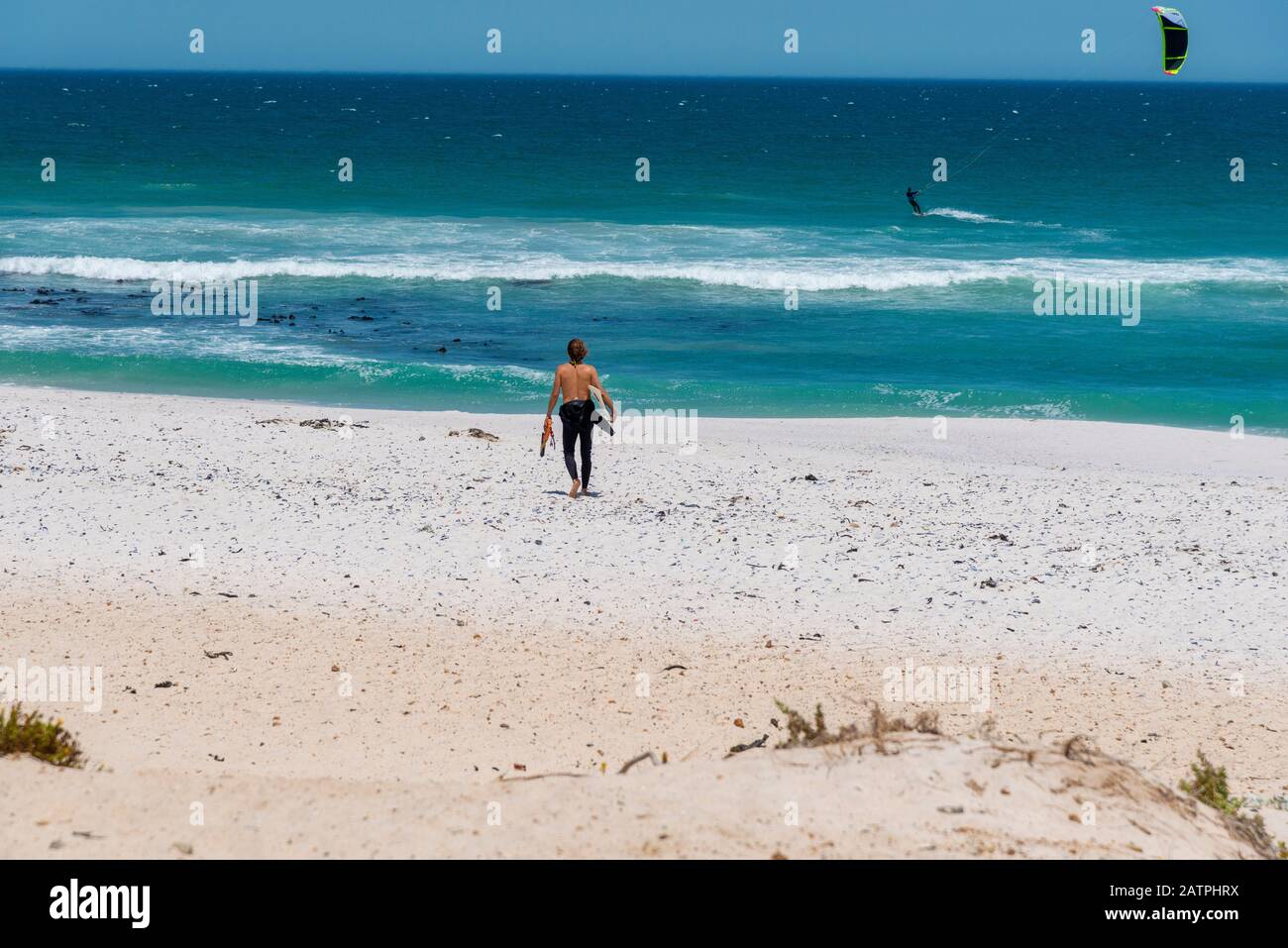 Surfer walks down sand at the famous, windy, kite surfing beach at Haakgat Point, Otto due Plessis Drive, Melkbosstrand,Capte Town, South Africa Stock Photo