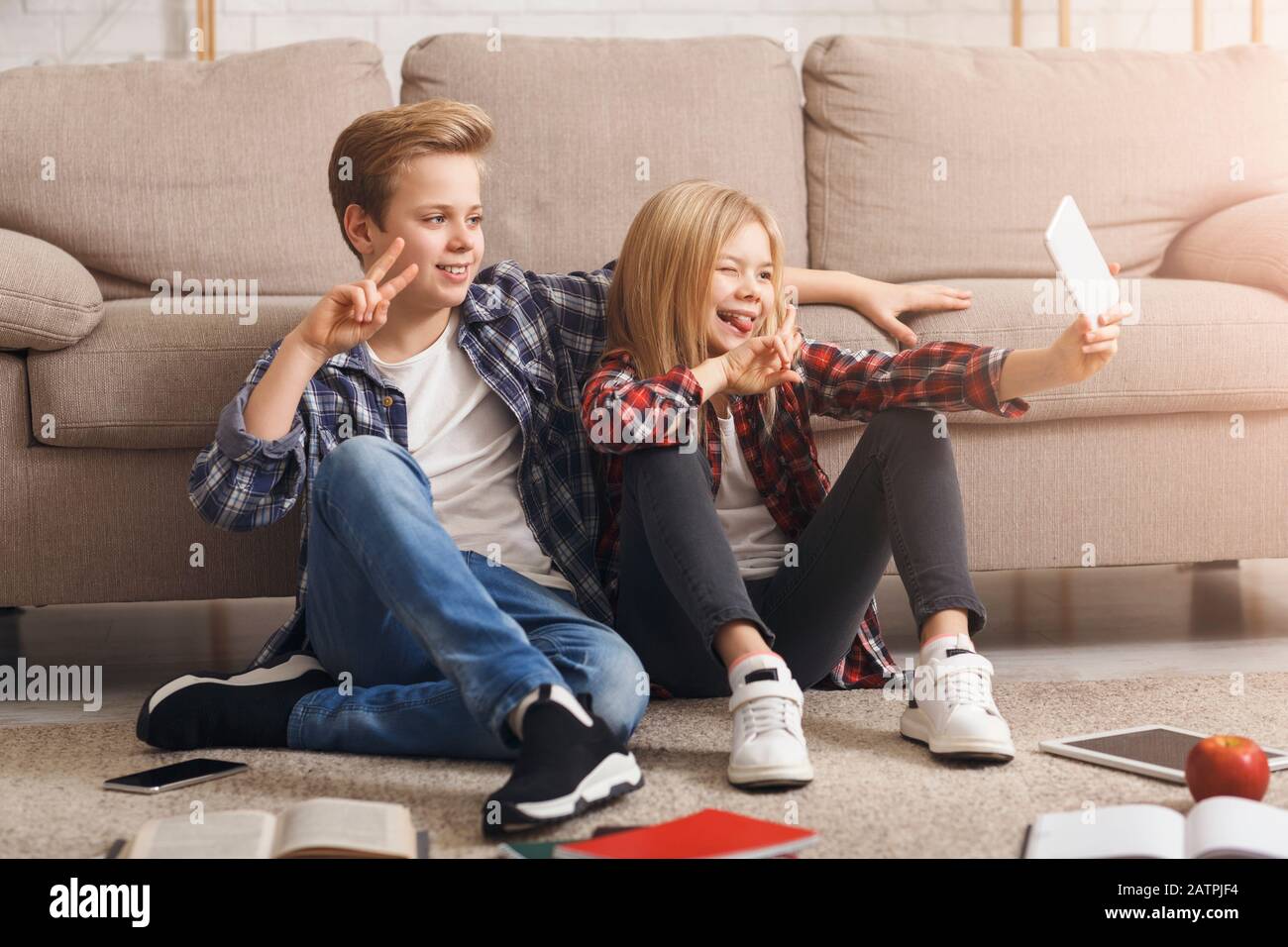 Brother And Sister Making Selfie Gesturing V-Sign Sitting On Floor Stock Photo
