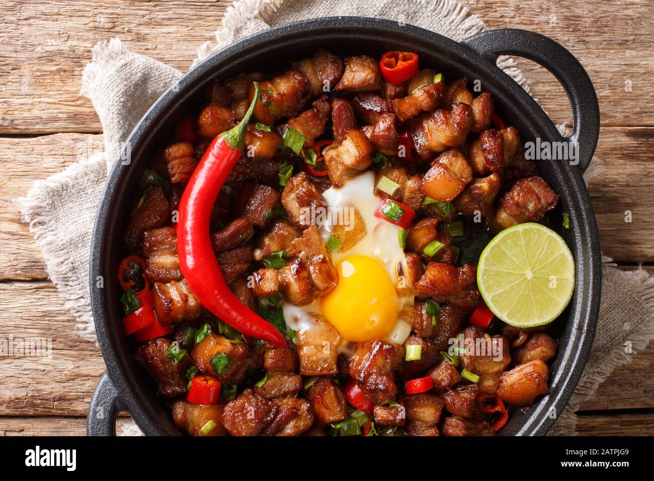 Sizzling spicy pork sisig with egg ang lime close-up in a pan on the table. Horizontal top view from above Stock Photo