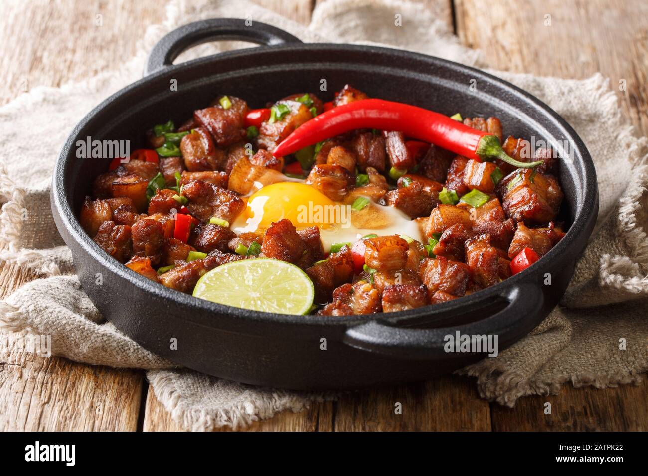 Tasty filipino sisig food served with egg, lime and chili pepper close-up in a pan on the table. horizontal Stock Photo