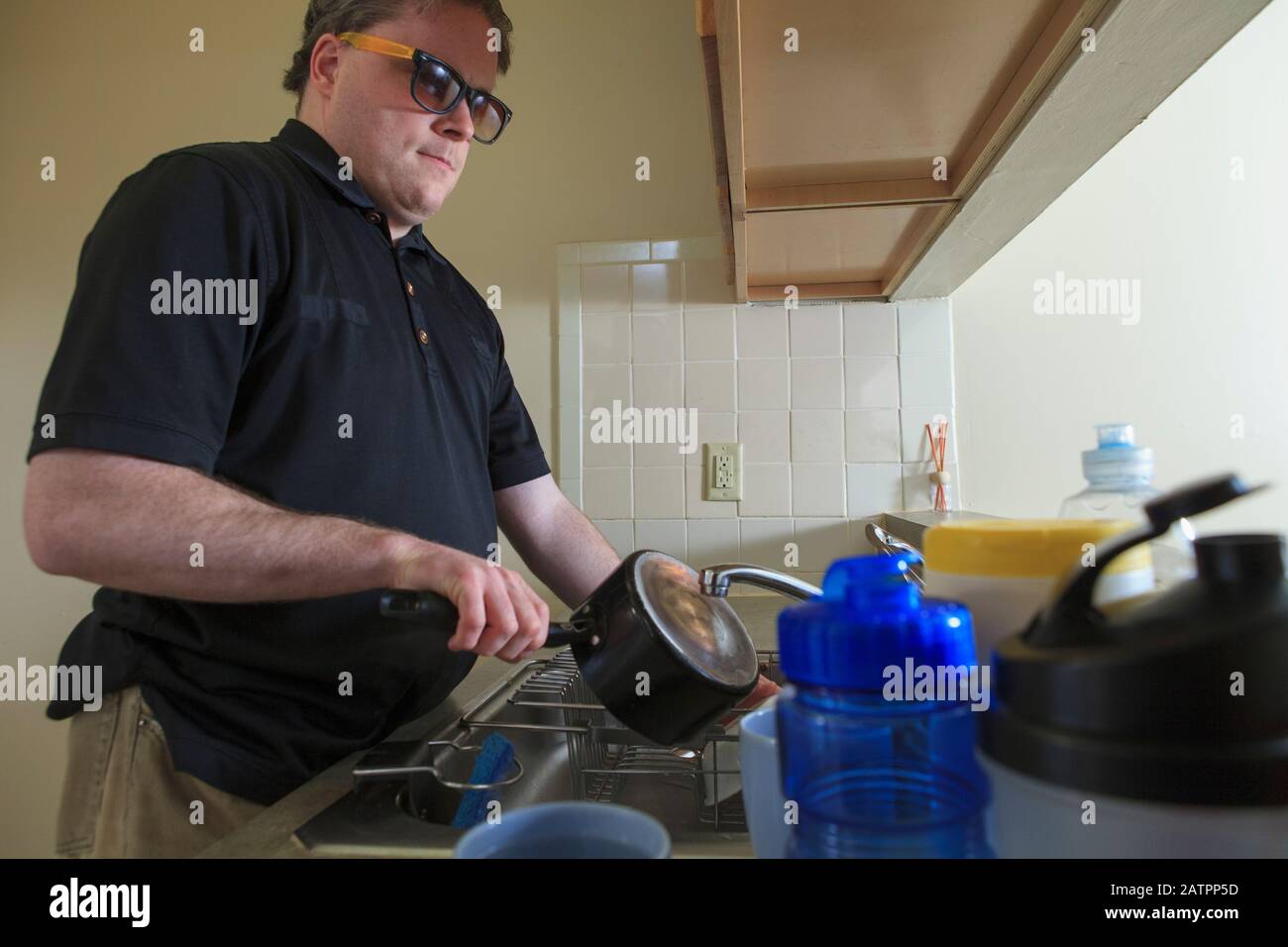 A man with a visual impairment stands at his kitchen sink washing