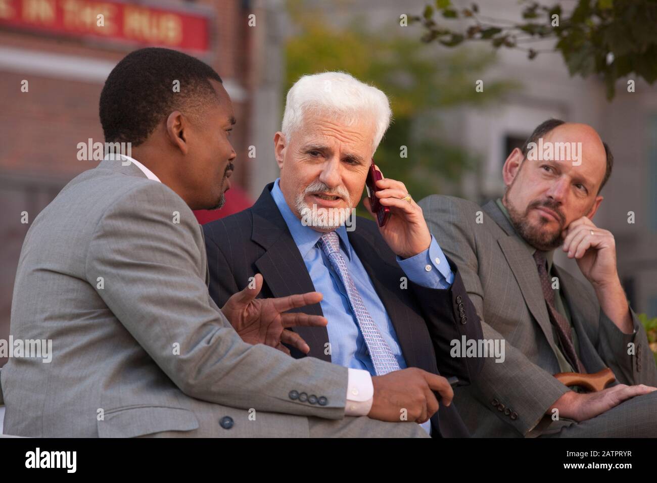Businessmen talking and sharing insights while one is on a cellphone Stock Photo