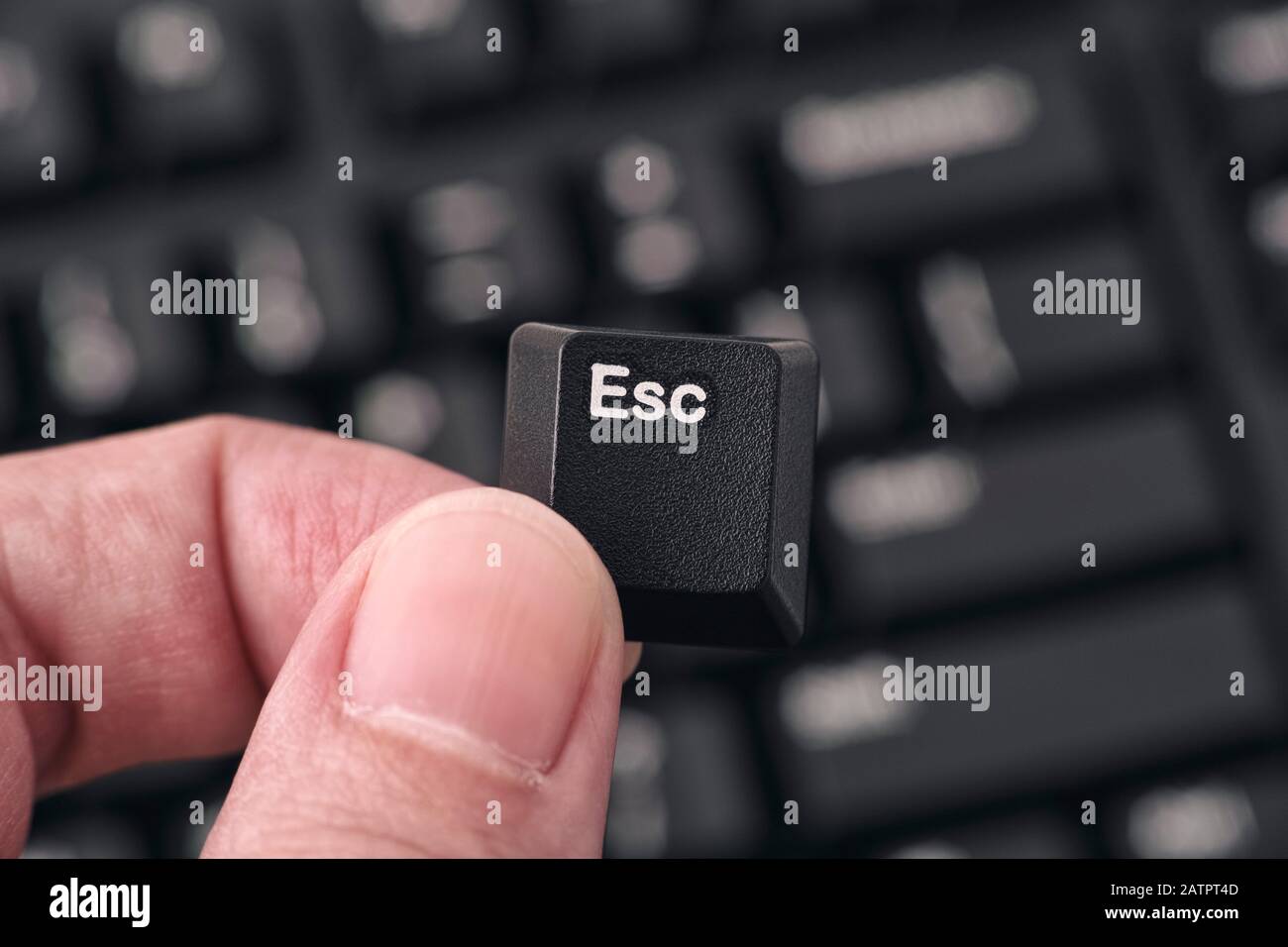 Man's hand holding Escape key against black keyboard. Closeup. Stock Photo