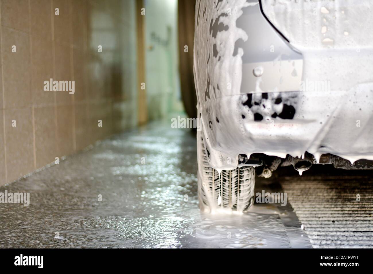 The car in soap foam, a fragment of the rear bumper and wheel, stands wraps on the soapy surface with a drain. Stock Photo
