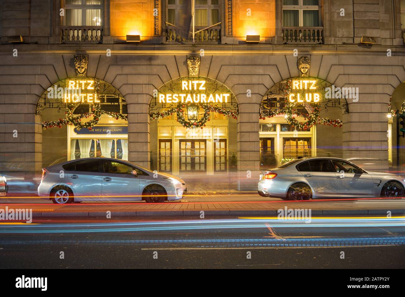 The Ritz Hotel and Restaurant lit up at night with Christmas decorations hanging. Long exposure with the lights of cars passing in front. London Stock Photo