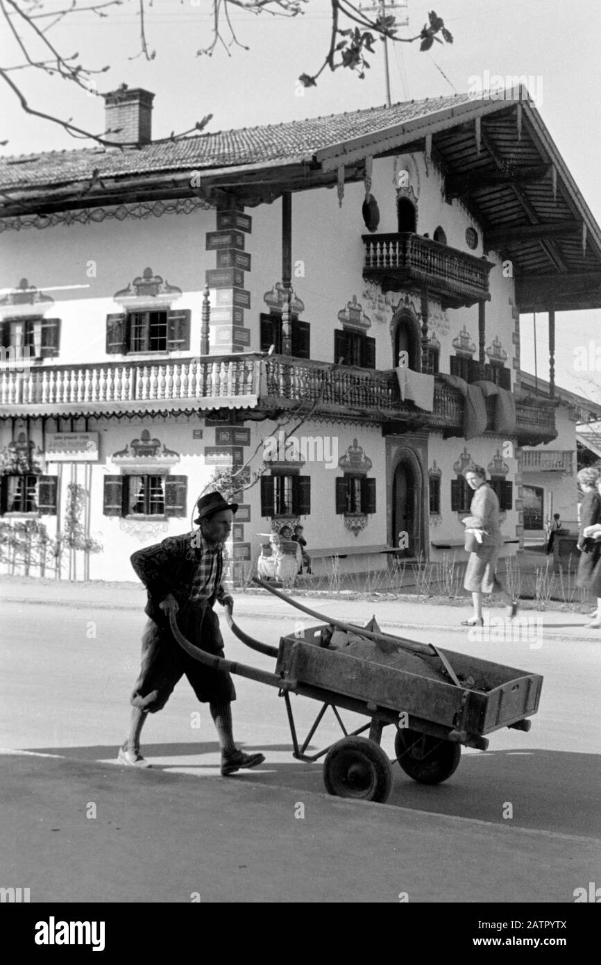 Mann mit Schubkarre vor typischem Wohnhaus, 1957. Man with wheelbarrow walking past dwelling of traditional construction style, 1957. Stock Photo