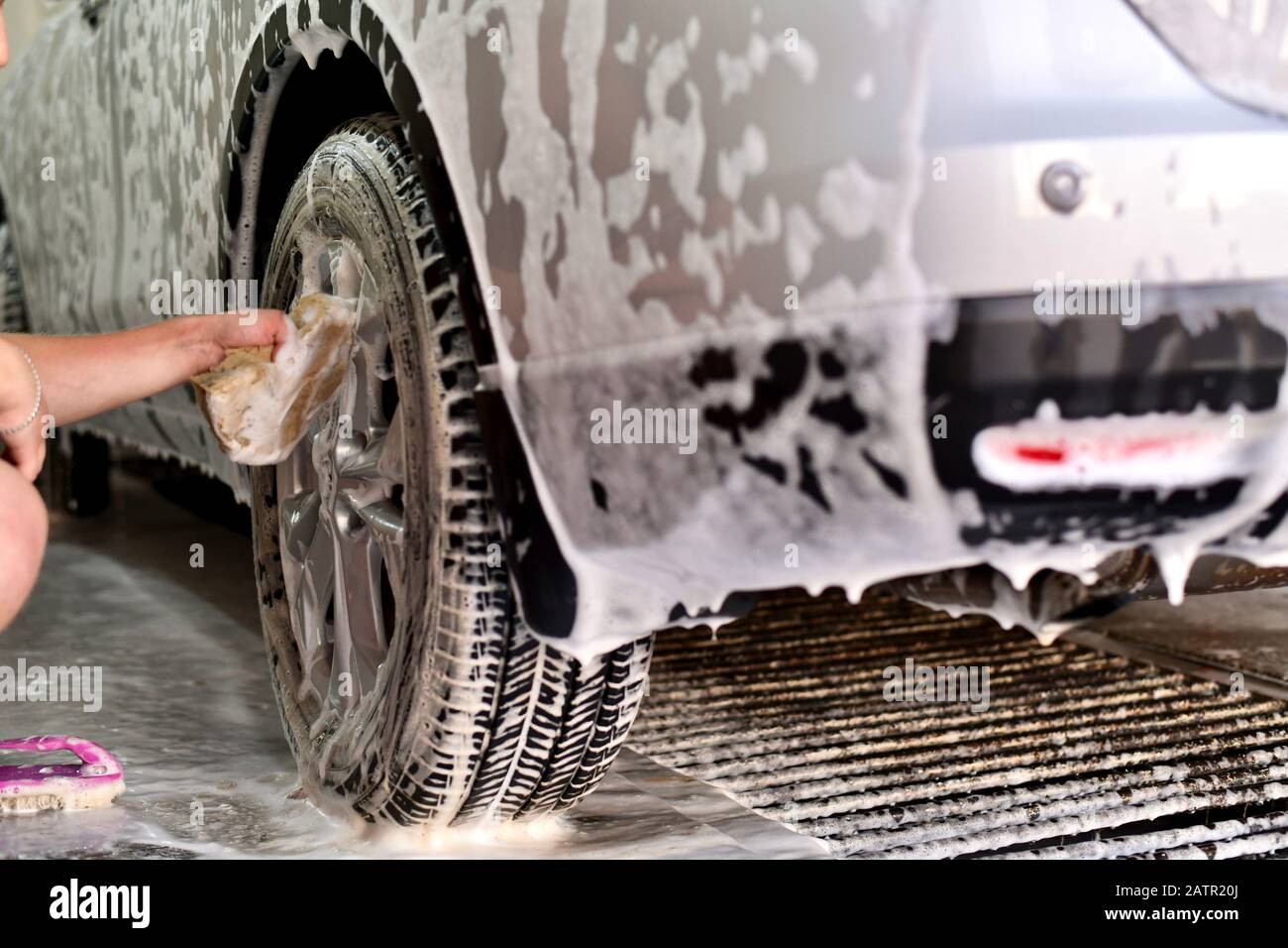 Hand a worker washing the top of a wheel disc, a fragment of the rear bumper of a car in soapy foam. Stock Photo