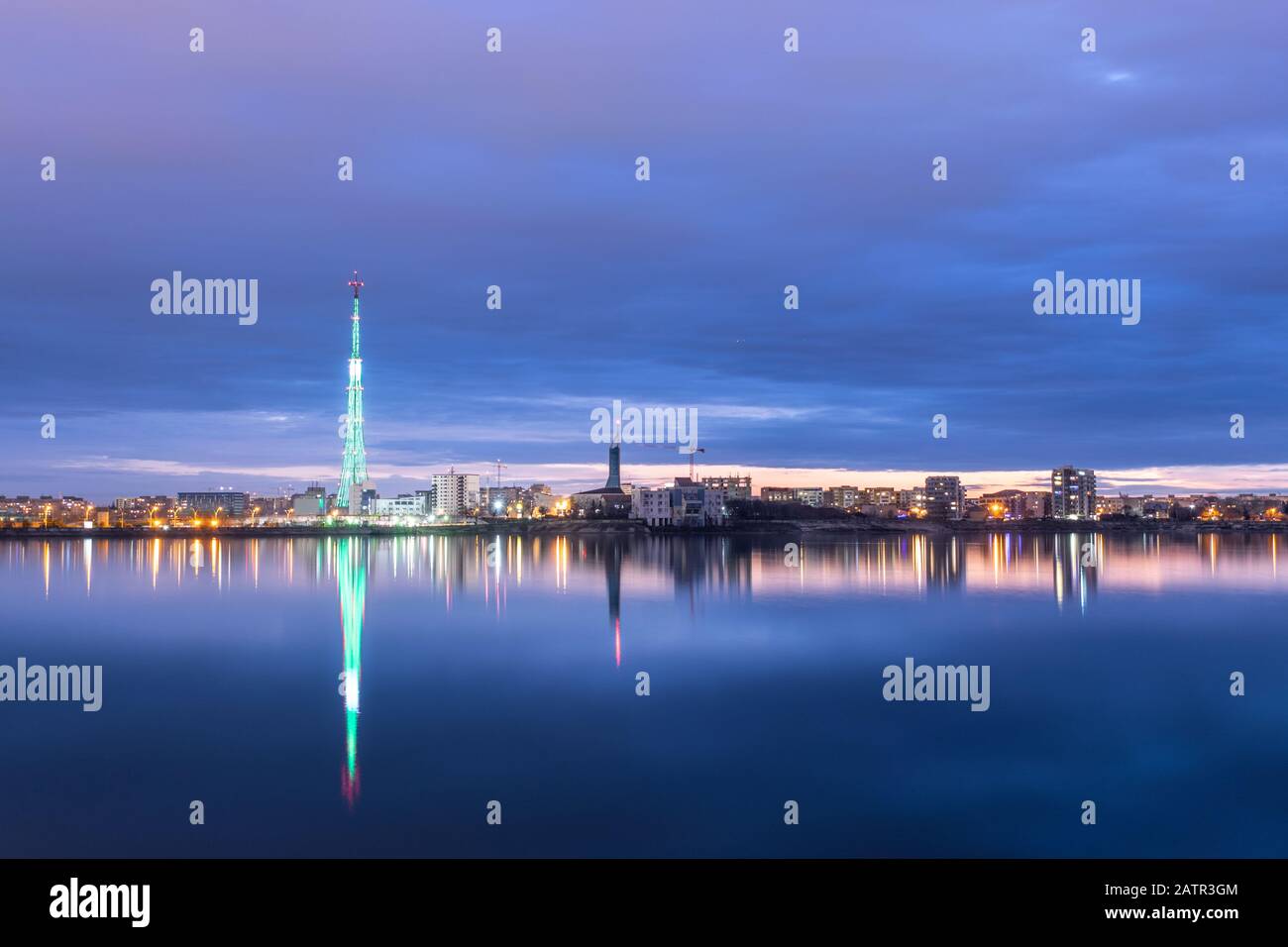 Long exposure photo of a beautiful sunset at Lacul Morii Lake with urban buildings in the background and a tower that looks like a Christmas tree - La Stock Photo