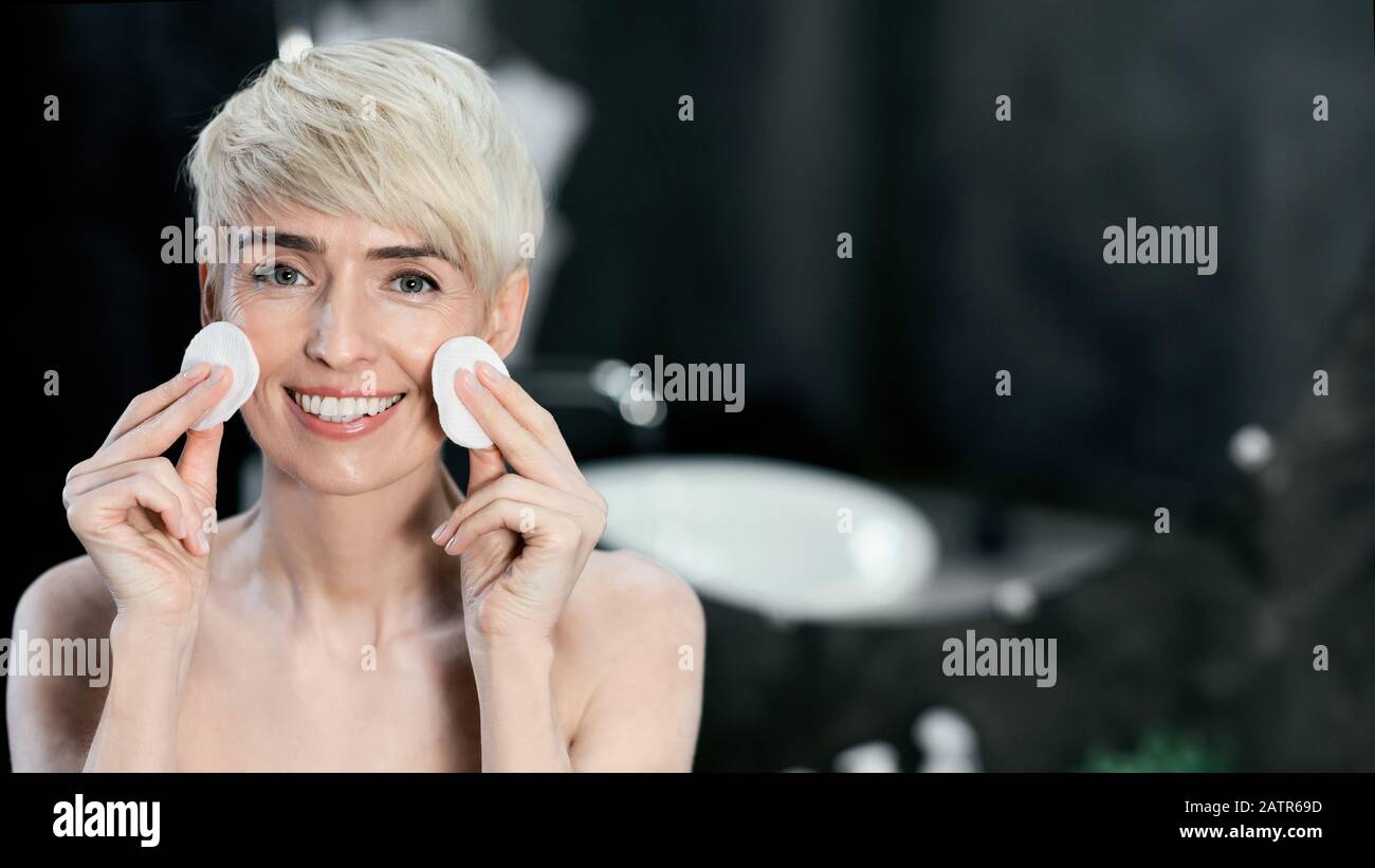 Mature Lady Holding Cotton Pads Near Eyes Standing In Bathroom Stock Photo