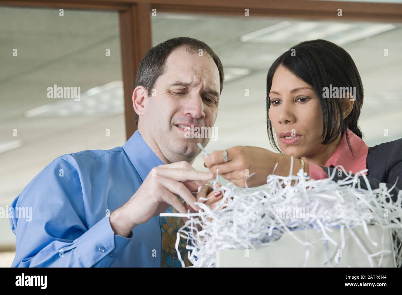 Businessman and businesswoman looking at shredded documents and trying to retrieve information from shreds Stock Photo