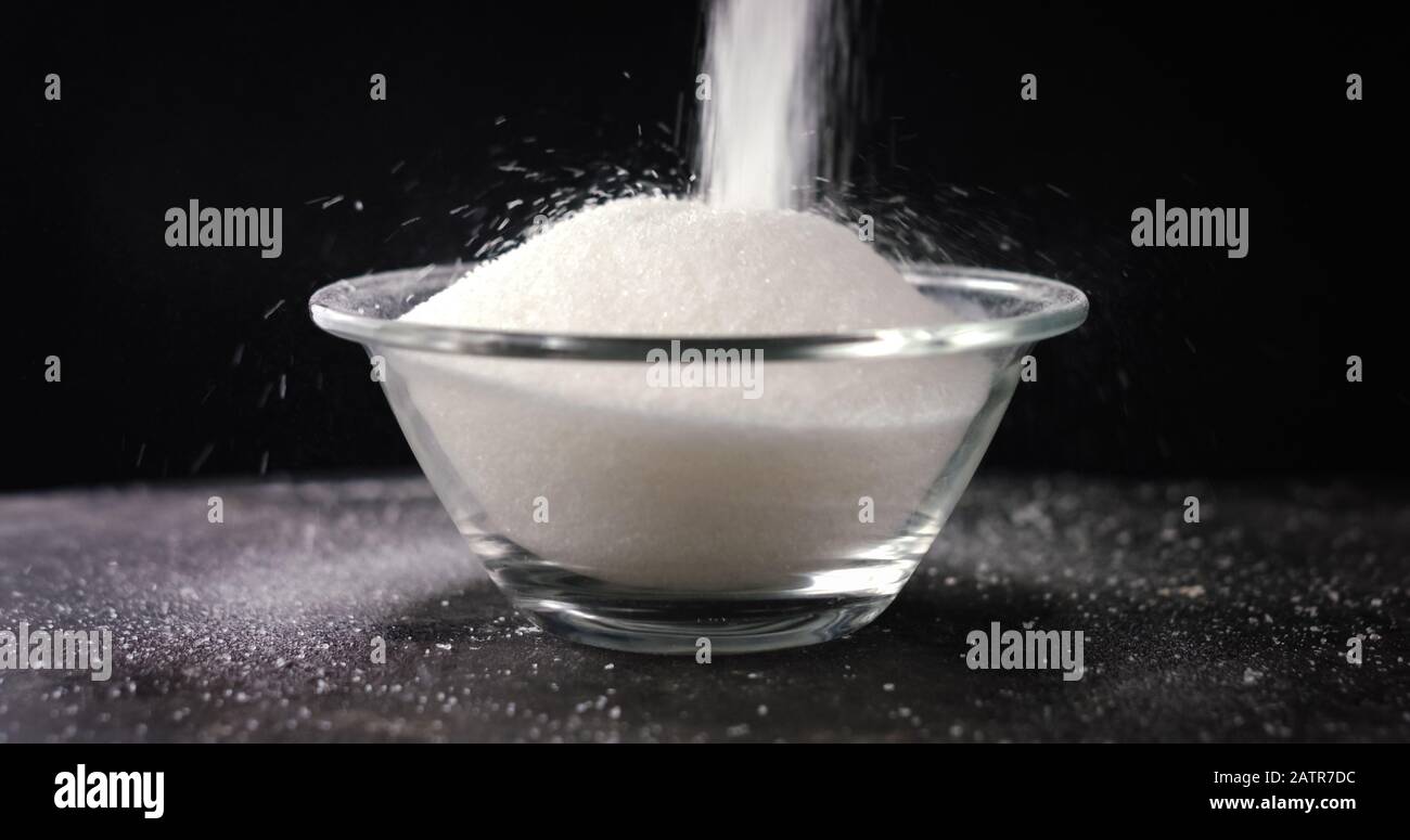 White sugar or salt falling in the bowl, black background Stock Photo