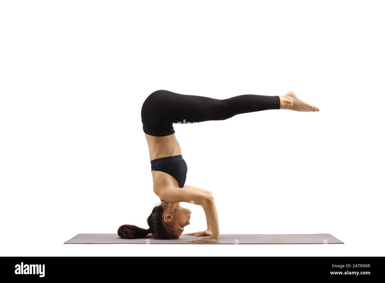 Young female in black top and leggings making a pose and standing on head isolated on white background Stock Photo