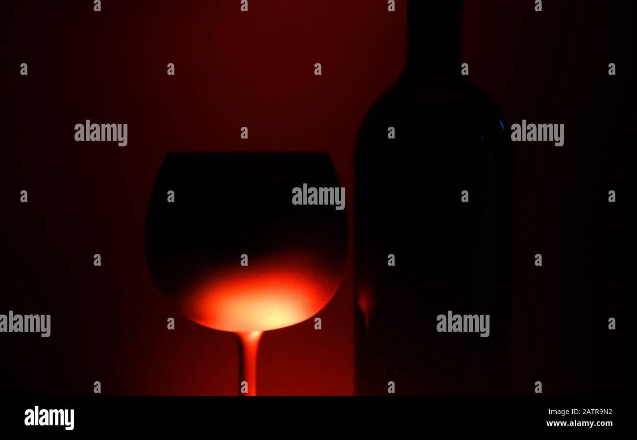 Close up of silhouette isolated wine glass and bottle illuminated by red shiny light, black background Stock Photo